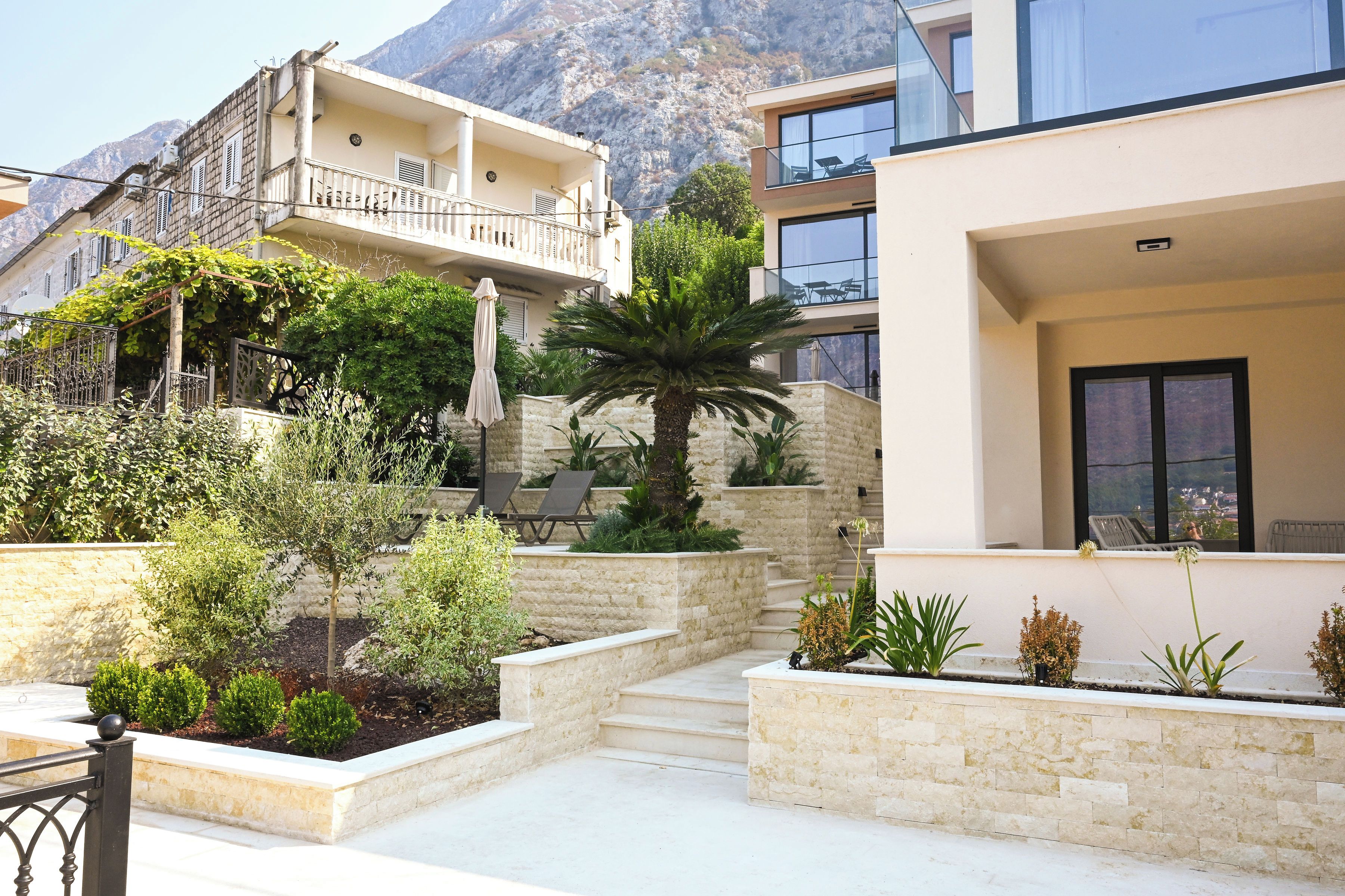 A residential area with a modern building, a balcony, and a garden with various plants and a palm tree.