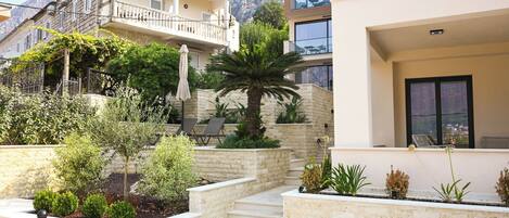 A residential area with a modern building, a balcony, and a garden with various plants and a palm tree.
