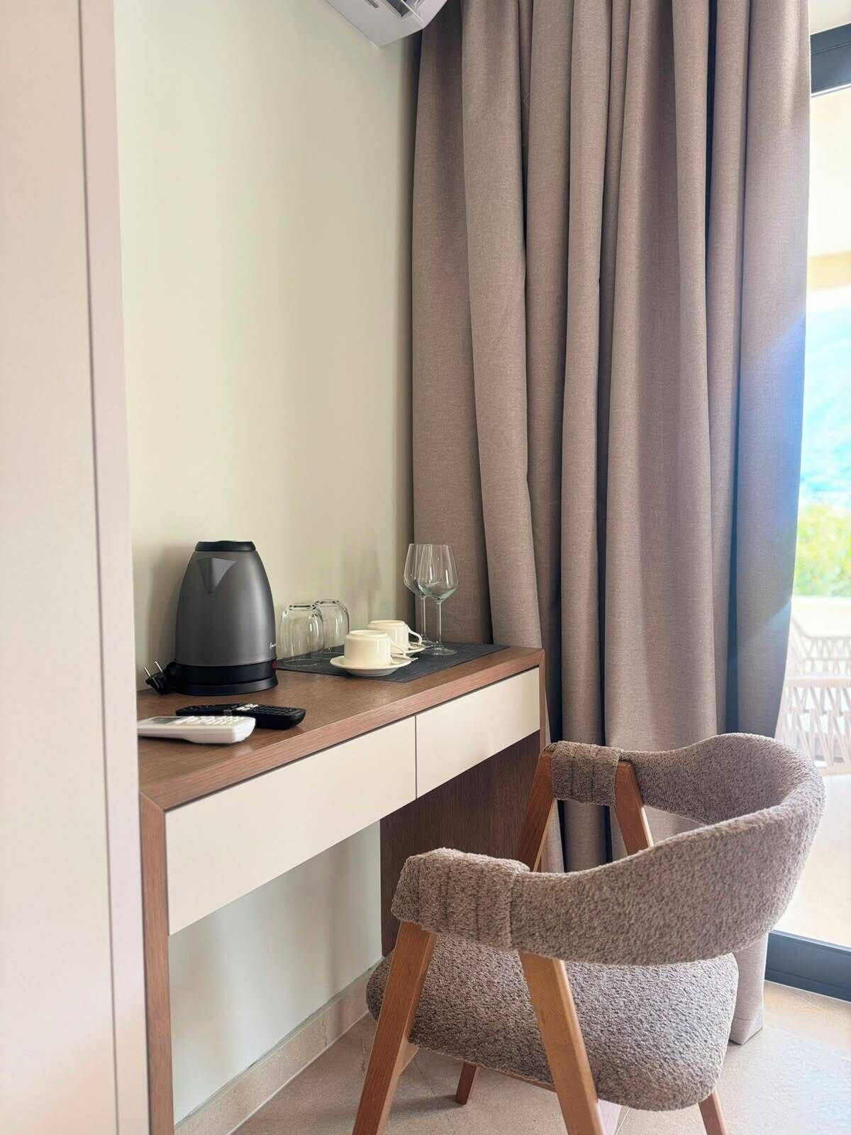 Habitación de hotel con escritorio, tetera, taza, vaso y silla.