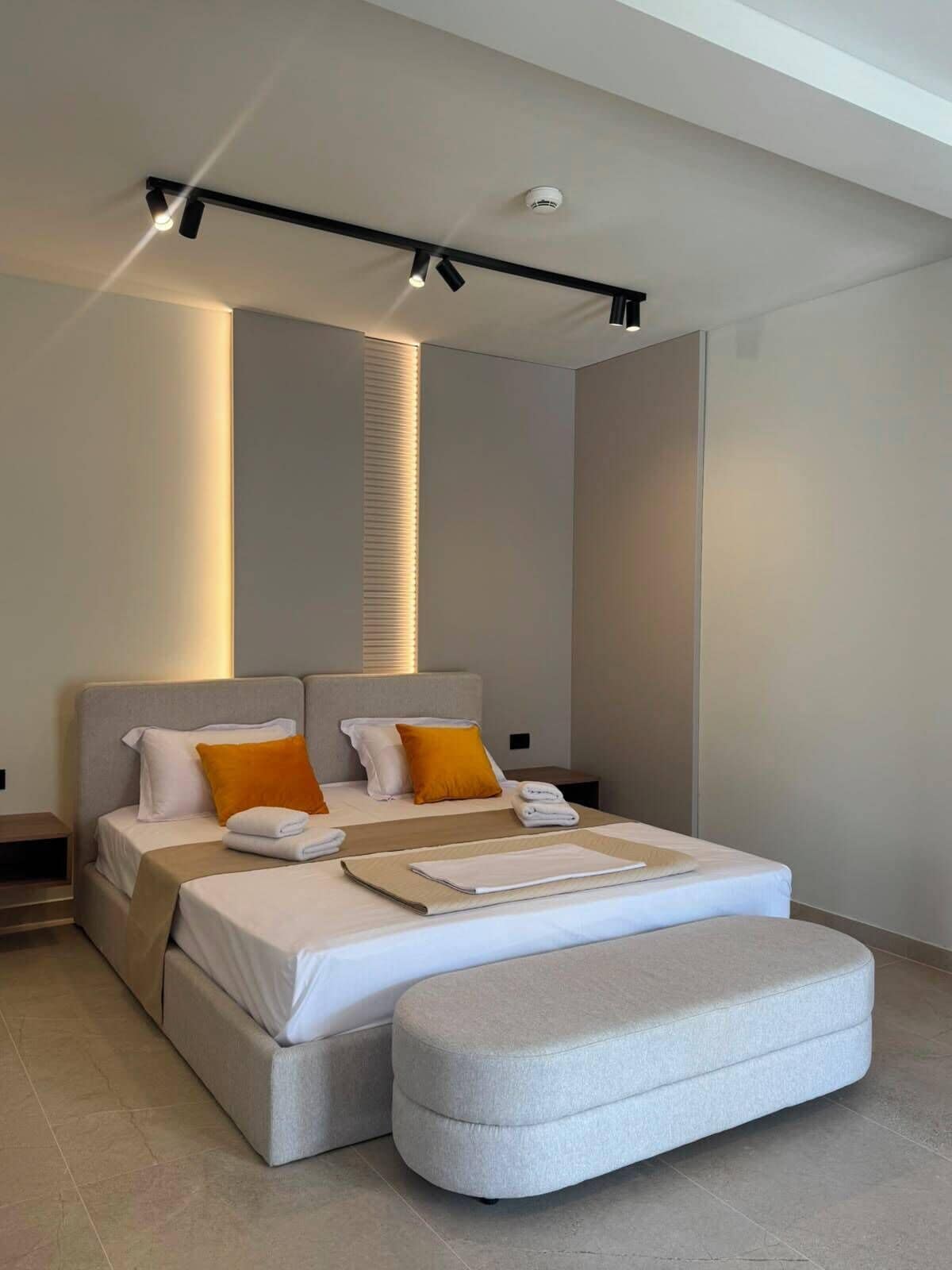 Quarto moderno com uma cama grande, duas mesas de cabeceira e um banco embutido.