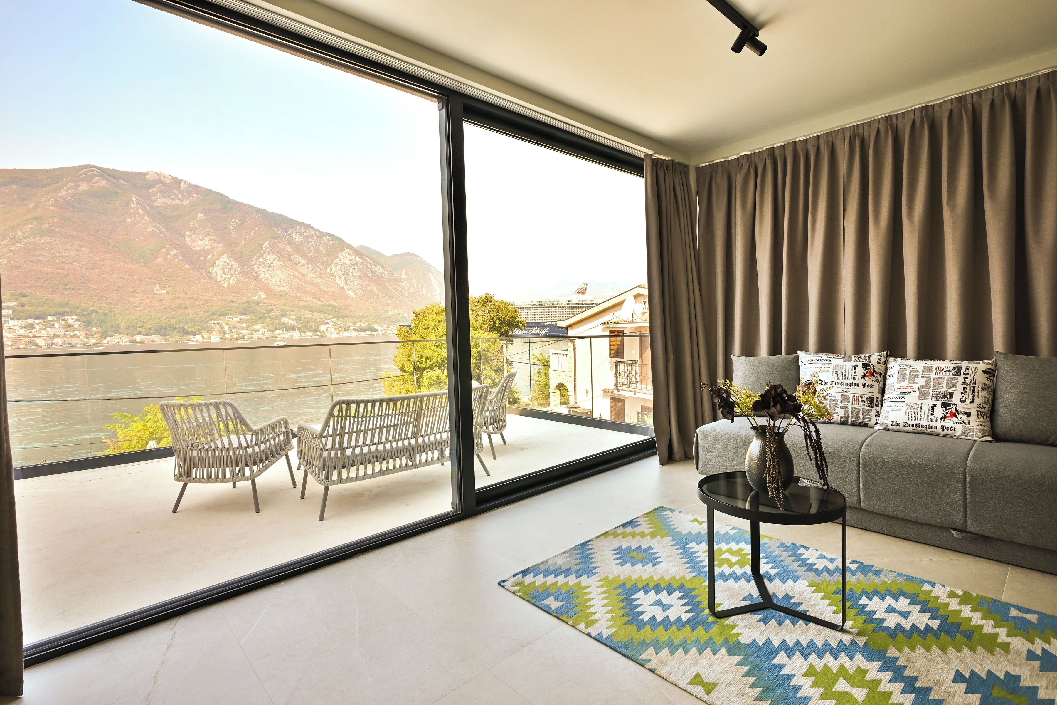 Un salon moderne doté d’une grande porte-fenêtre coulissante donnant sur un balcon avec vue sur une rivière et des montagnes.