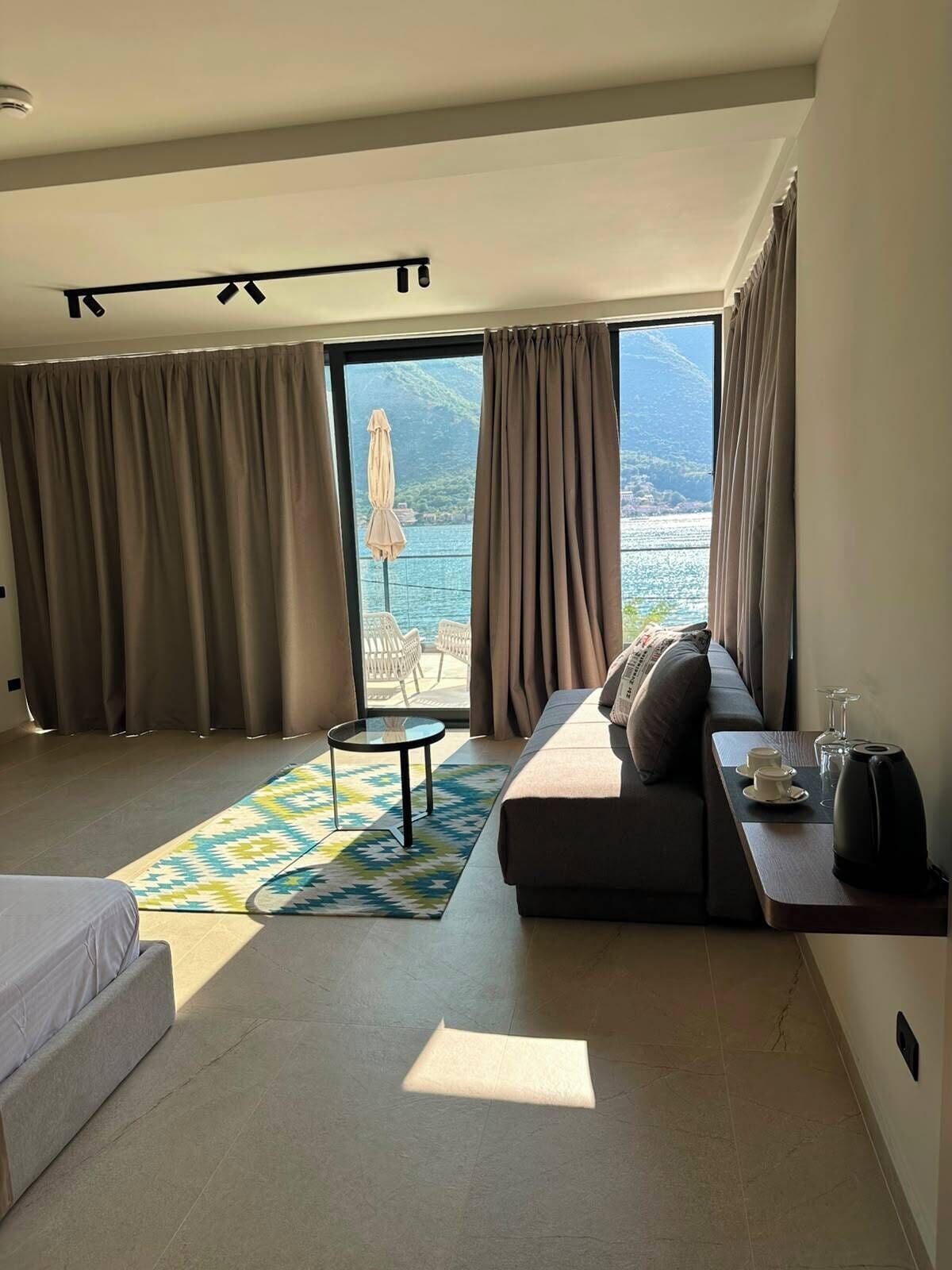 Quarto de hotel moderno com sofá, mesa pequena, cama e vista para o mar.