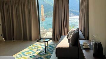Quarto de hotel moderno com sofá, mesa pequena, cama e vista para o mar.