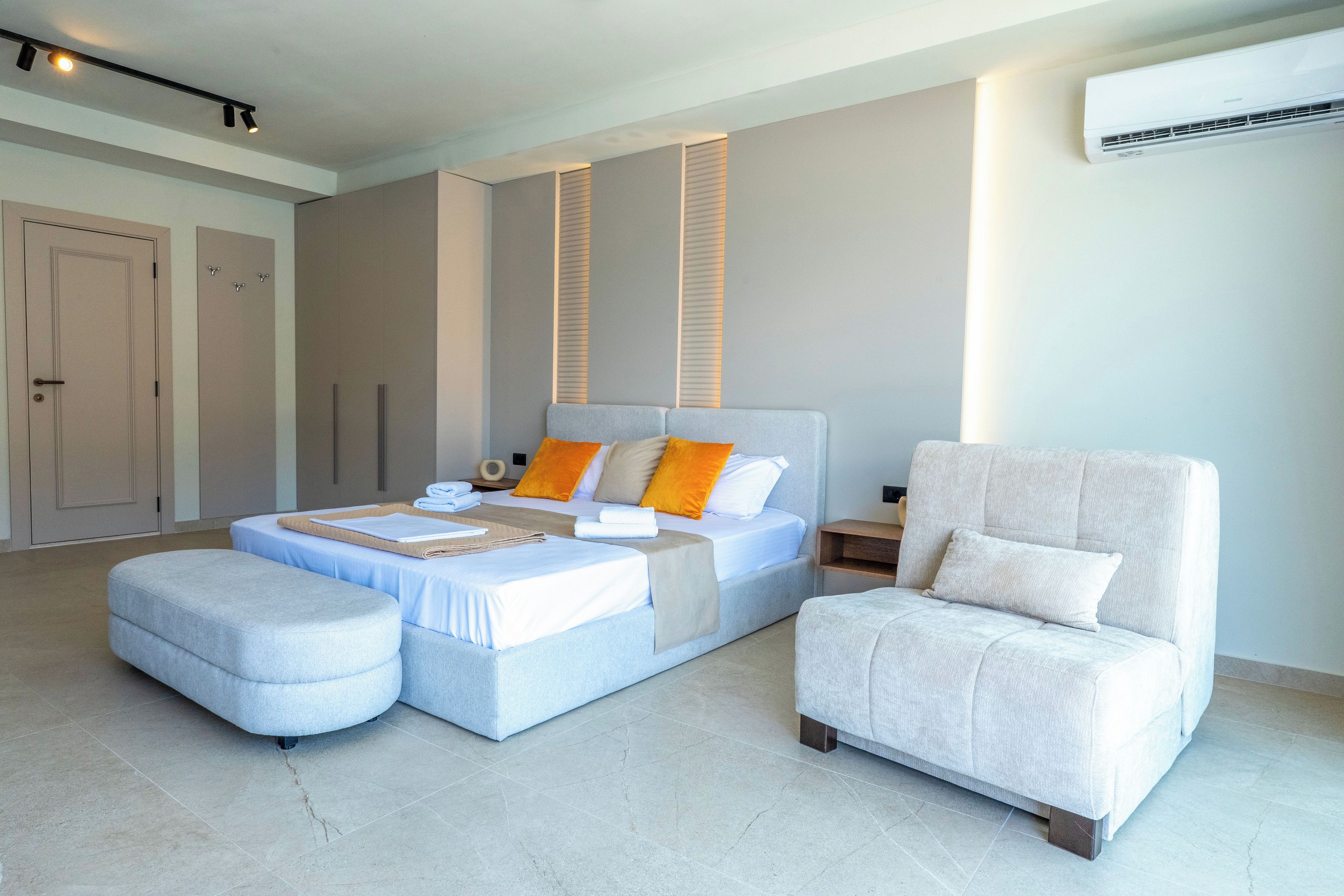 Une chambre à coucher moderne avec un lit, deux poufs, une chaise et un appareil de climatisation.