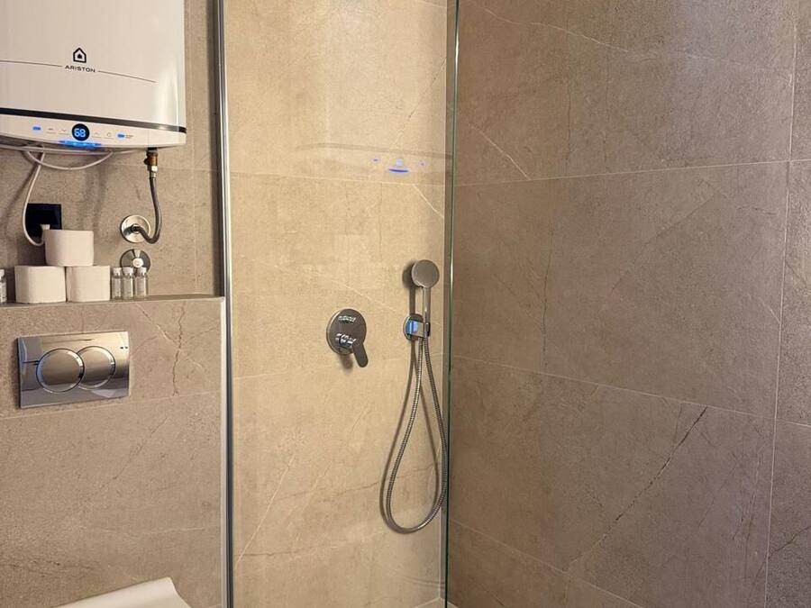 A modern bathroom with a glass-enclosed shower, a toilet, and a wall-mounted water heater.
