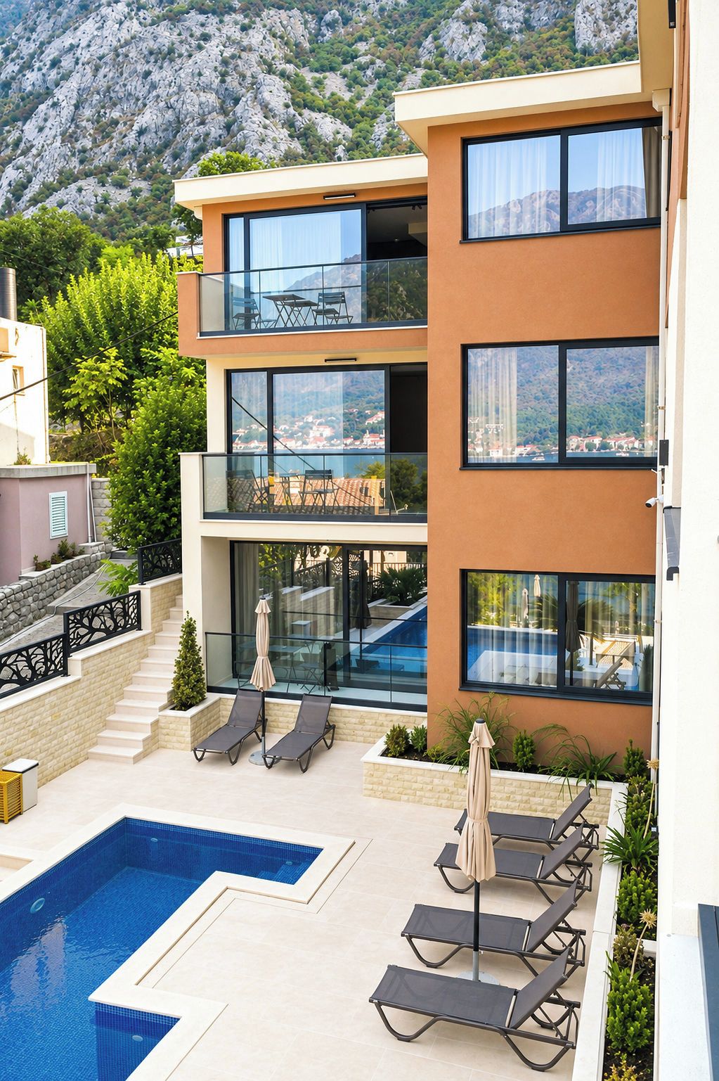 Un edificio moderno de varios pisos con piscina, mobiliario exterior y vistas a un paisaje montañoso.
