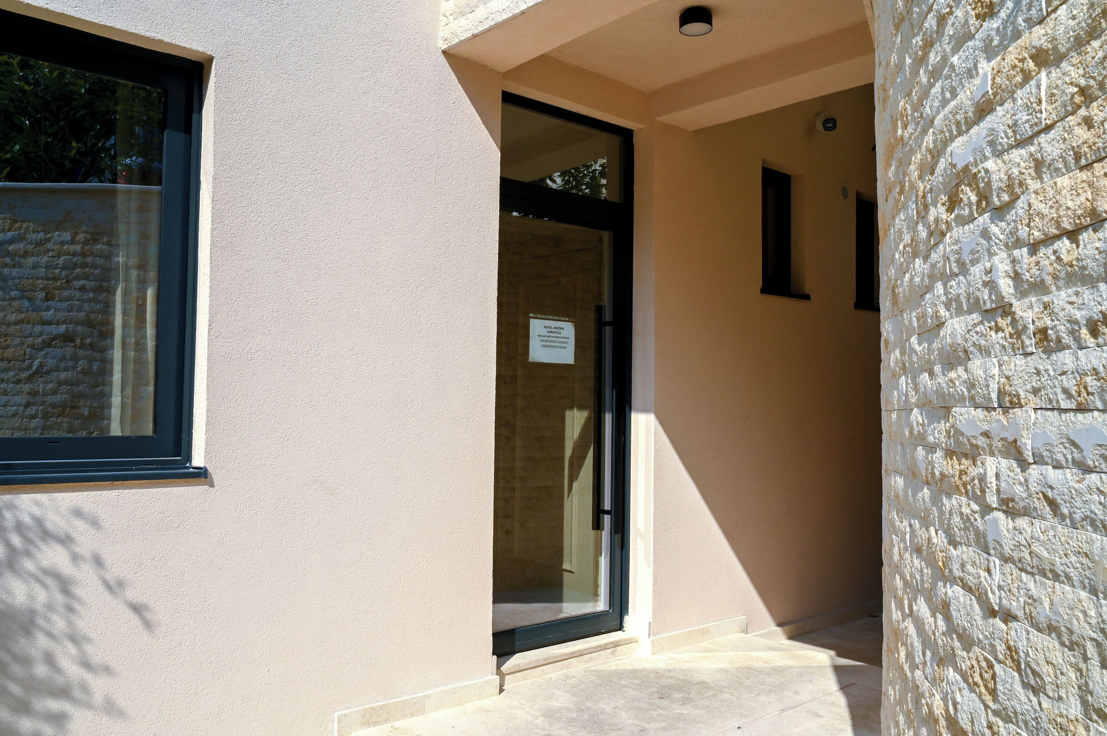 Entrada de hotel con puerta de cristal, pared de piedra y una ventana.