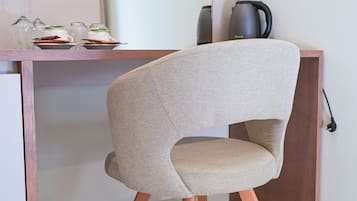 Una silla moderna con respaldo tejido y patas de madera, ubicada frente a un escritorio con una computadora portátil y un hervidor.
