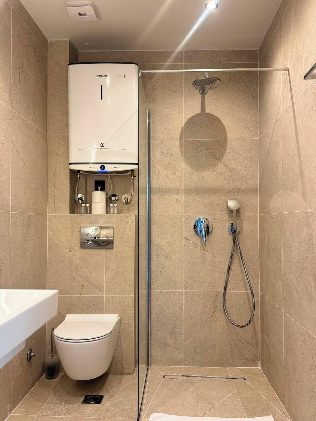 Une salle de bain moderne équipée de toilettes, d’une douche avec un pommeau de douche amovible et d’un radiateur mural.