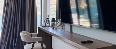Una habitación moderna con un televisor de pantalla plana grande, un escritorio con una silla y vistas a un paisaje montañoso a través de amplios ventanales.