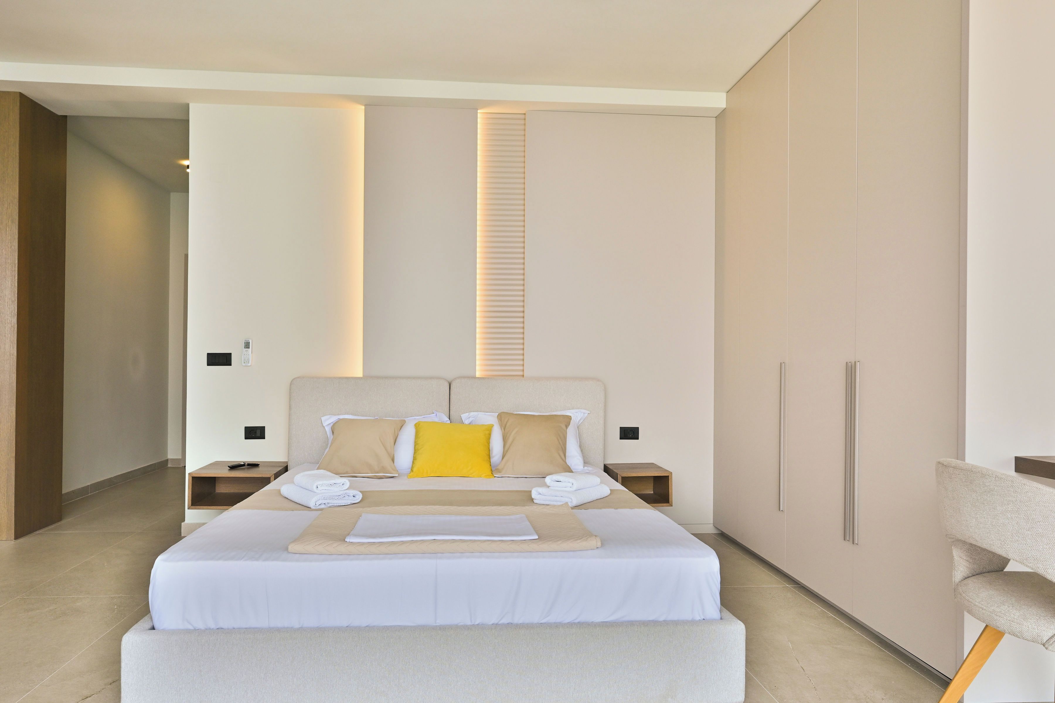 Una habitación de hotel moderna con una cama grande, mesitas de noche, una silla y un armario.