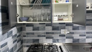 A kitchen with a gas stove, a dish rack, and shelves with glassware and jars. - Cozy House + Kitchen + AC + Pet-Friendly + TV + WiFi @ Cali (Cali)