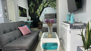 A modern living room with a grey sofa, a glass coffee table, a white dresser, and a large tree mural on the wall. - Cozy House + Kitchen + AC + Pet-Friendly + TV + WiFi @ Cali (Cali)