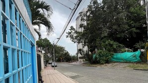 A street view with a sidewalk, a blue building with a grid pattern, and a road with a green tarp on the right. - Cozy House + Kitchen + AC + Pet-Friendly + TV + WiFi @ Cali (Cali)