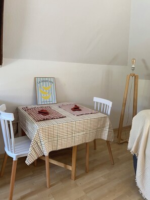 A dining area with a checkered tablecloth, white chairs, a framed picture on the wall, and a floor lamp.