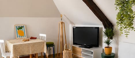 Ein gemütliches Schlafzimmer im Loft-Stil mit schrägem Dach, einem Holzesstisch, einem Fernseher und einem Bett mit einem gestreiften Kopfkissen in Weiß und Gelb.