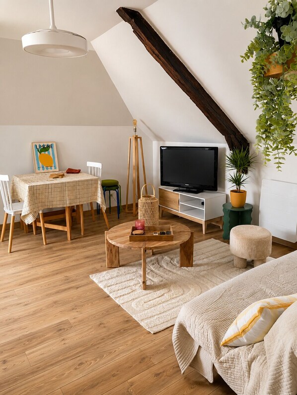 A cozy loft bedroom with a sloped ceiling, a wooden dining table, a TV, and a bed with a white and yellow striped pillow.