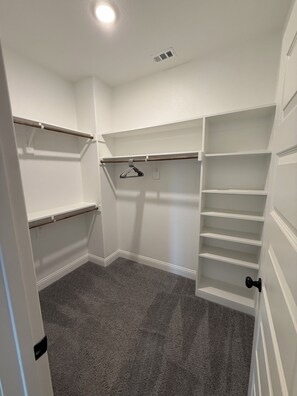A walk-in closet with white walls, grey carpet, and multiple shelves and hanging rods. - Modern 3BR Home Near Hospital & Navarro College (Corsicana)