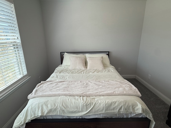 A bedroom with a bed, white bedding, a window with blinds, and a carpeted floor.