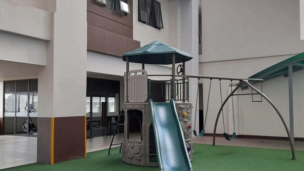 A playground with a slide and swings, located in an indoor area with a high ceiling and large windows. - Cozy Retreat by Jane, UNIT 626 (Cebu City)
