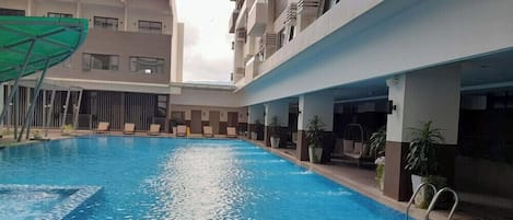 A swimming pool with lounge chairs and potted plants, surrounded by a multi-story building with balconies.