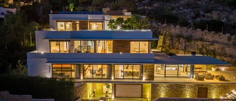 A modern two-story house with large windows, a stone facade, and a landscaped front yard.