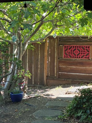 A wooden fence with a decorative panel, a tree with hanging ornaments, and a potted plant. - Urban Refuge in a welcoming East Bay  Neighborhood (Oakland)