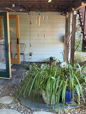 A covered outdoor area with a wooden ceiling, a chair, a potted plant, and a wall with hanging light fixtures. - Urban Refuge in a welcoming East Bay  Neighborhood (Oakland)