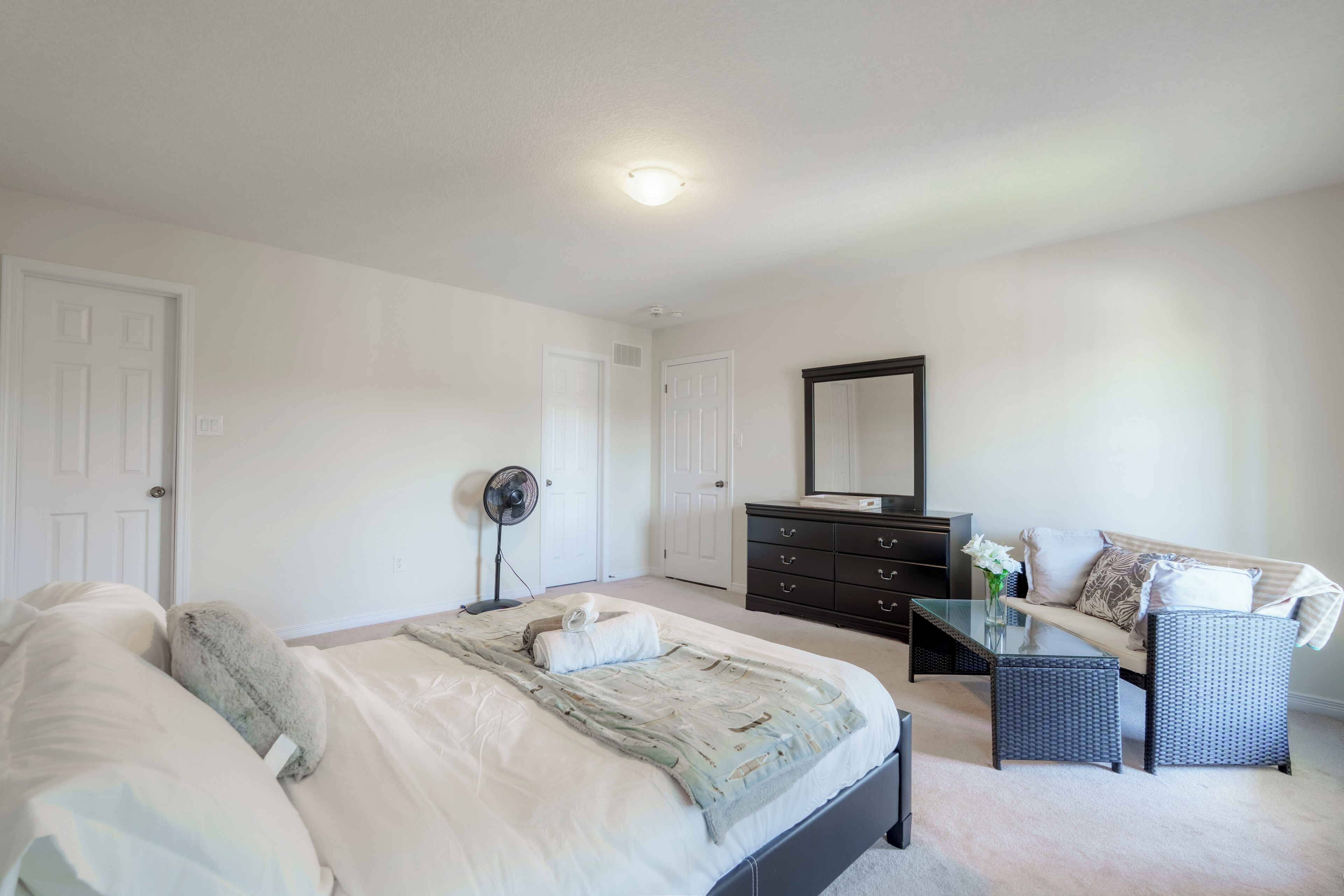 A bedroom with a bed, dresser, mirror, and seating area.