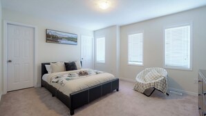 A bedroom with a bed, a chair, a dresser, and a window with blinds. - Luxury 4BR Getaway|Mins to Falls & Casino|Sleeps 9 (Niagara Falls)