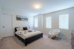 Ein Schlafzimmer mit einem Bett, einem Sessel, einem Schminktisch und einem Fenster mit Jalousien.
