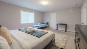 A bedroom with a bed, a bedside table, a window with blinds, a door, and a carpeted floor. - Luxury 4BR Getaway|Mins to Falls & Casino|Sleeps 9 (Niagara Falls)
