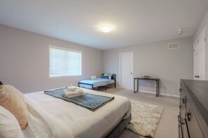 A bedroom with a bed, a bedside table, a window with blinds, a door, and a carpeted floor.