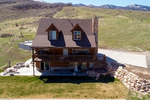A two-story log cabin with a stone chimney, a balcony, and a patio with outdoor furniture. - Family Cabin with Beautiful view of Bear Lake (Garden City)