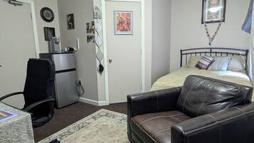 A bedroom with a bed, a desk, a chair, and a refrigerator.