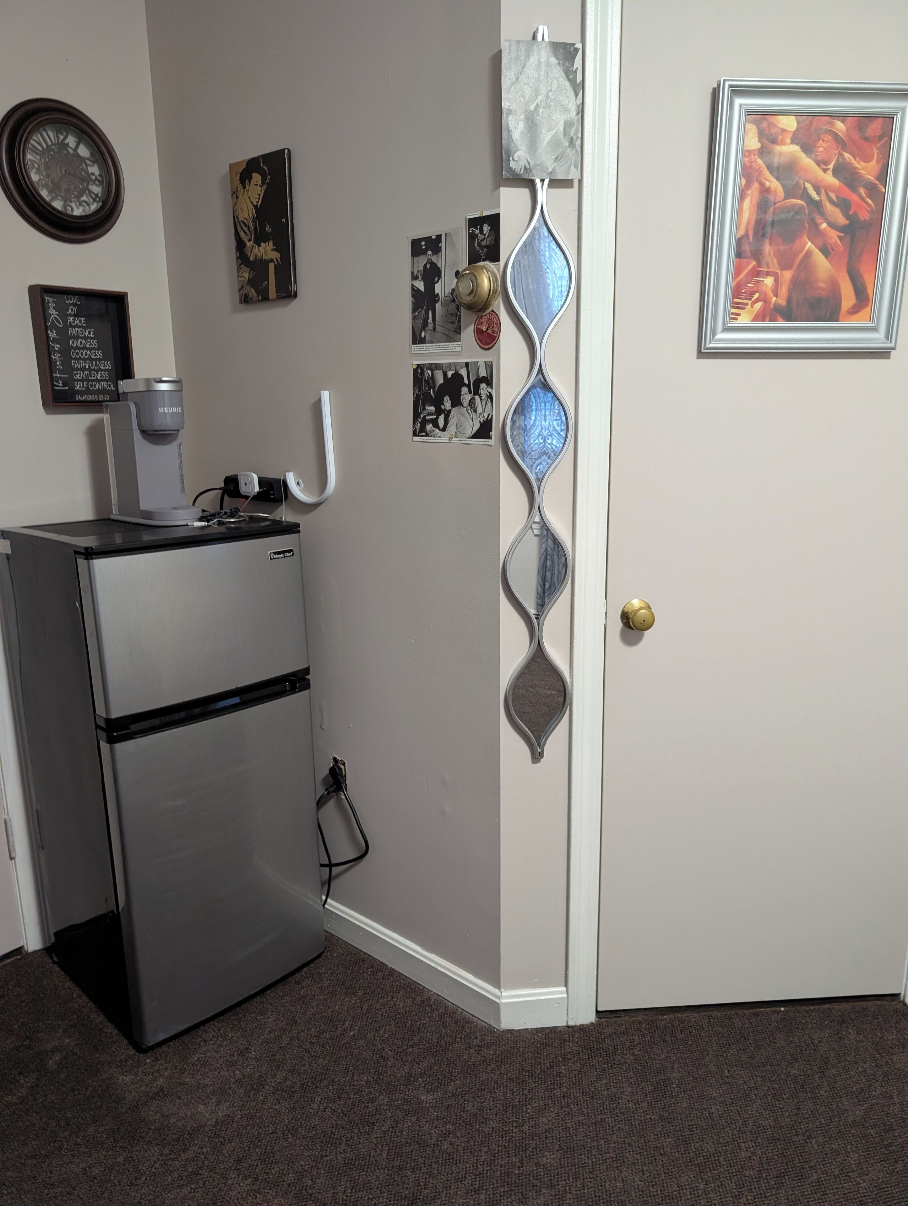 A kitchen with a refrigerator, a coffee maker, and wall decorations including a clock and framed pictures.