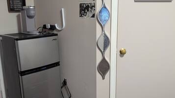 A kitchen with a refrigerator, a coffee maker, and wall decorations including a clock and framed pictures.