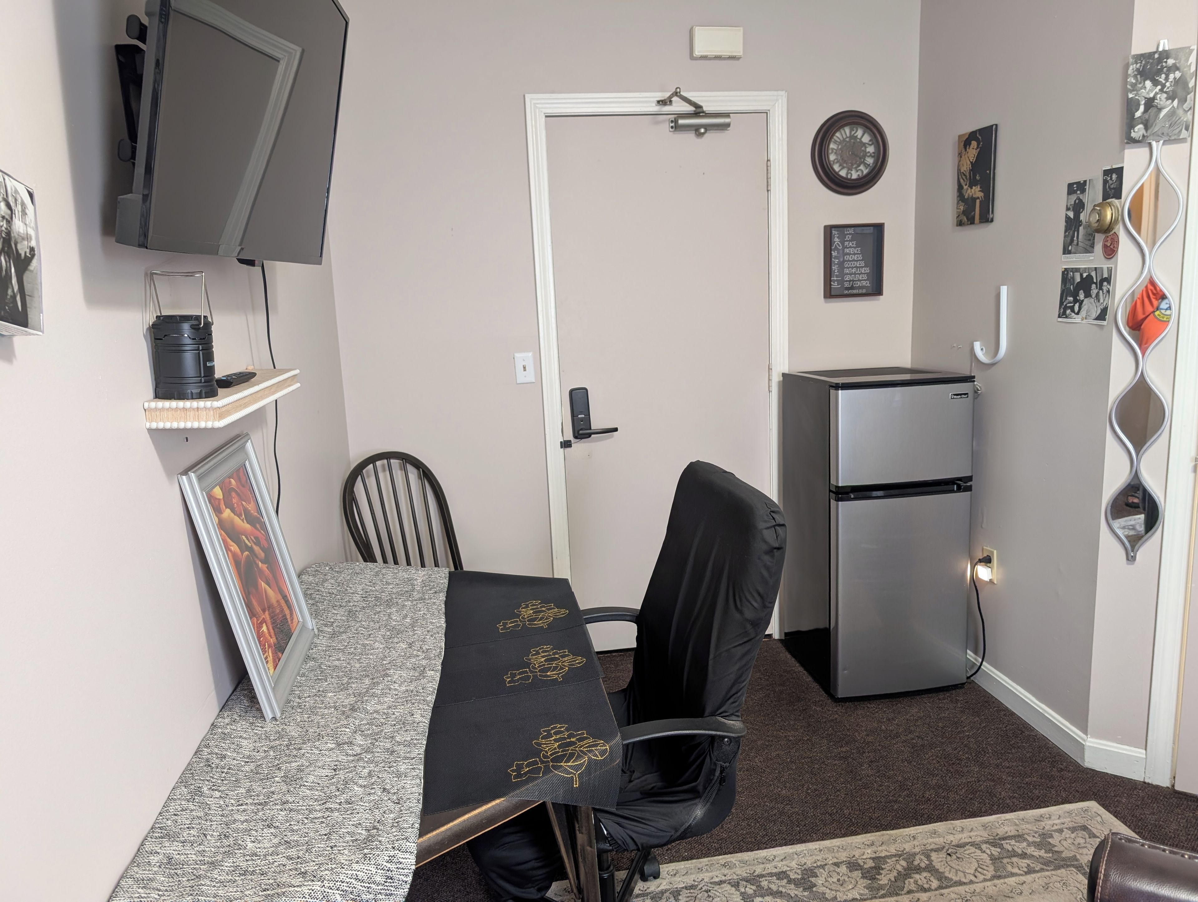 A compact living space with a kitchenette, a dining area with a table and chairs, a television mounted on the wall, and a refrigerator.