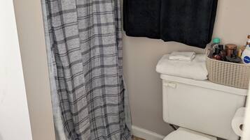 A bathroom with a white toilet, a black towel, a grey plaid shower curtain, and a black bath mat.
