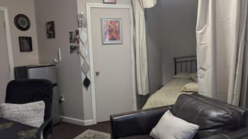 Una habitación con un sofá de cuero, una mesita, una cama con cortina a rayas y una puerta con un tirador decorativo.