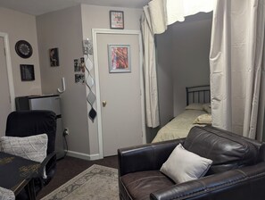 Ein Zimmer mit einer Ledersofa, einem kleinen Tisch, einem Bett mit einer Streifenvorhang und einer Tür mit einem dekorativen Griff.