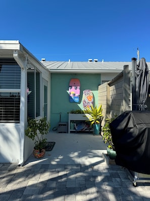 A backyard with a covered grill, potted plants, a white table, and a surfboard mural on the wall. - Tranquil 2-bedroom waterfront house in charming Matlacha (Matlacha)