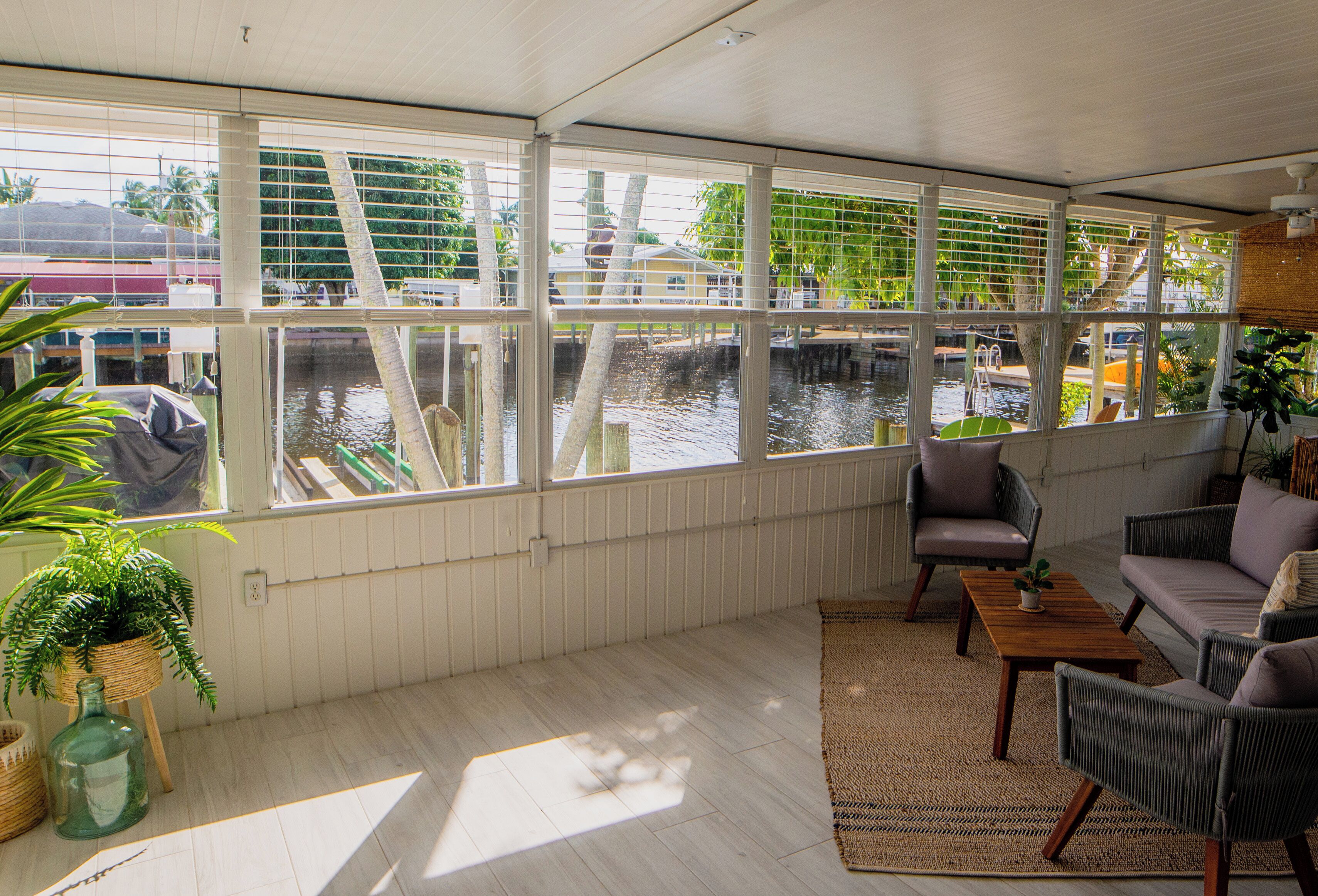 A room with large windows overlooking a water body, furnished with a sofa, chairs, and a small table.
