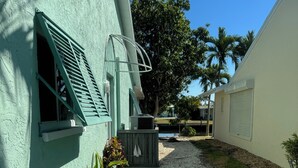 Um caminho leva a um edifício com fachada verde e uma janela com persianas.
