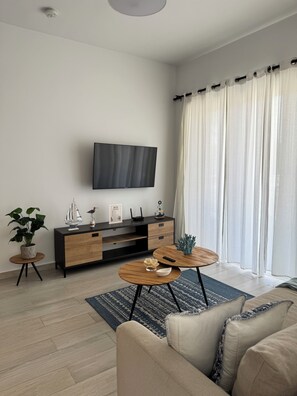 Ett modernt vardagsrum med en platt-TV som är monterad på väggen, ett träskåp med lådor, ett runt soffbord, en soffa och en krukväxt.