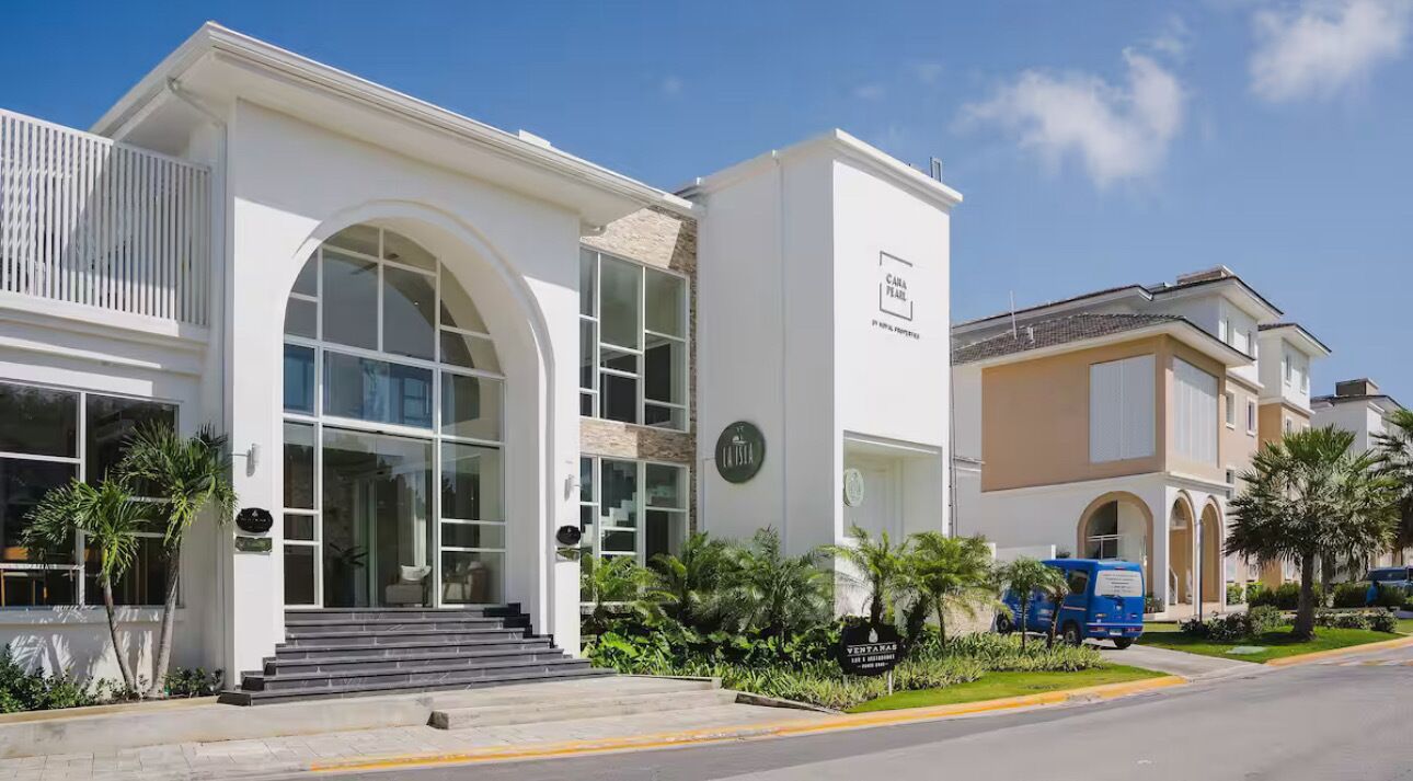 A modern hotel with a white facade, large arched windows, and a blue van parked in front.