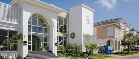 A modern hotel with a white facade, large arched windows, and a blue van parked in front.