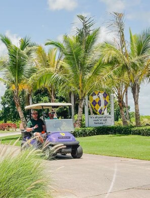 A golf cart with two people, palm trees, and a sign with a quote. - Cozy 1-bedroom apartment in superb Punta Cana with AC (Punta Cana)