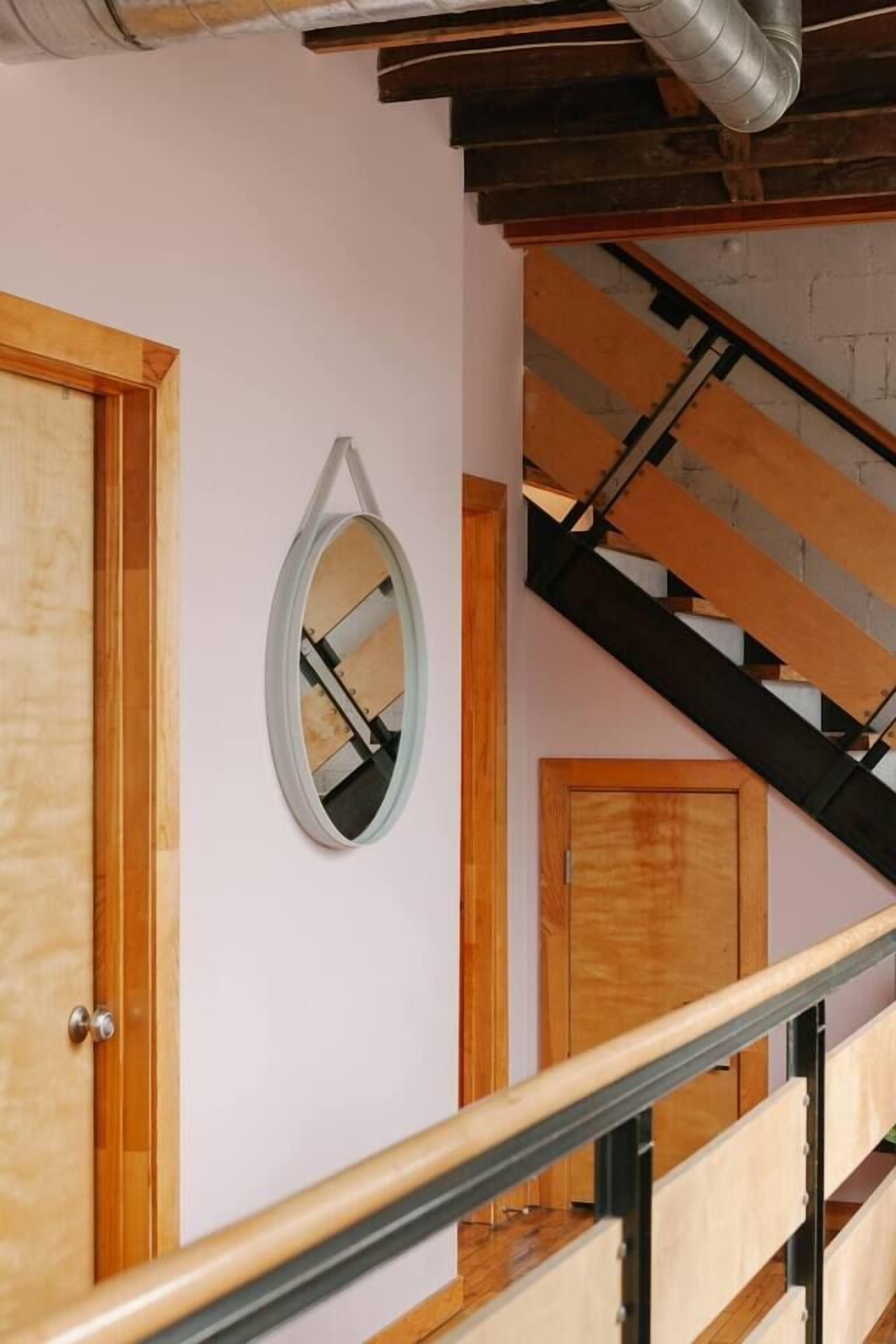 Una escalera de madera con barandillas metálicas que lleva a un rellano con una puerta de madera y un espejo fijado a la pared.