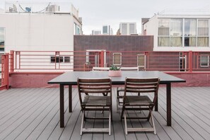 A rooftop terrace with a table and chairs, a potted plant, and a view of buildings.